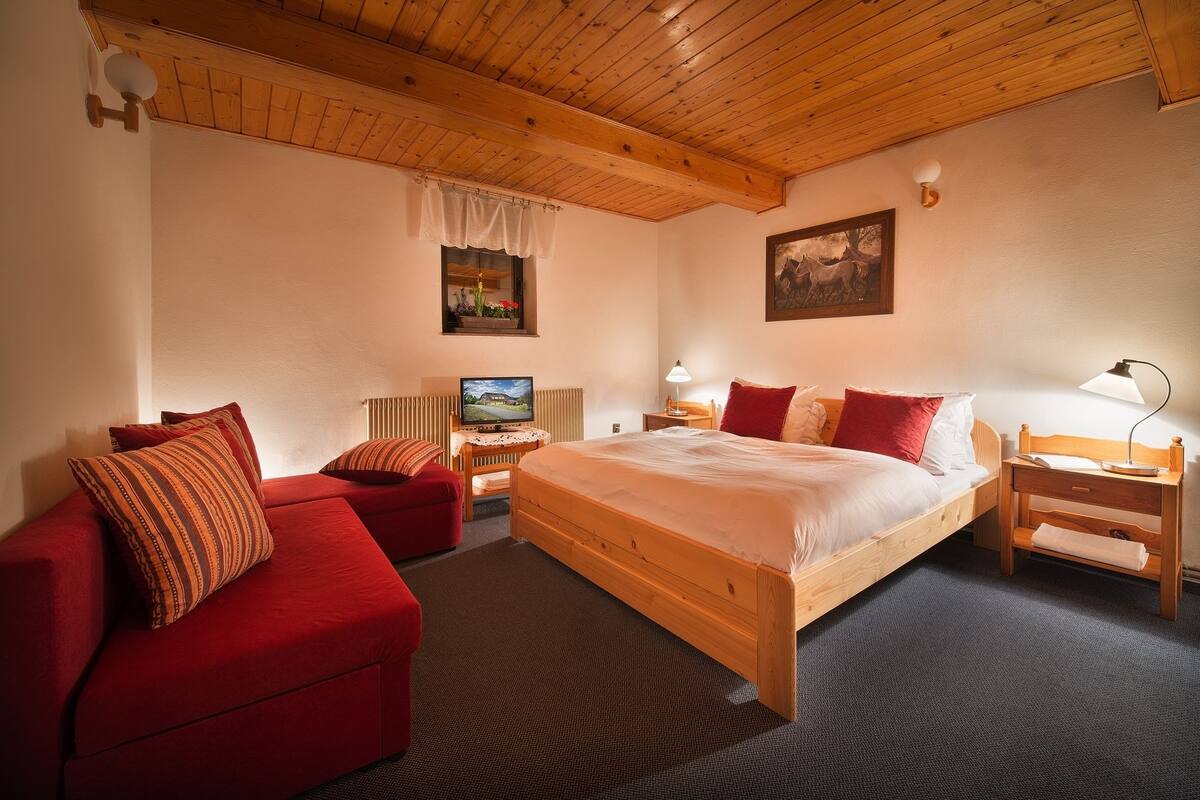 A cozy room with a large bed, a red sofa, a wooden nightstand, and a television.