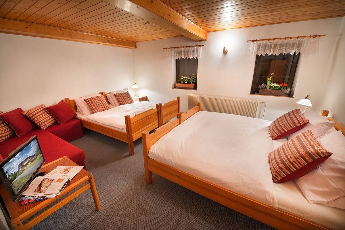A hotel room with two wooden beds, a red sofa, a small table with a laptop and brochures, and two windows with curtains.