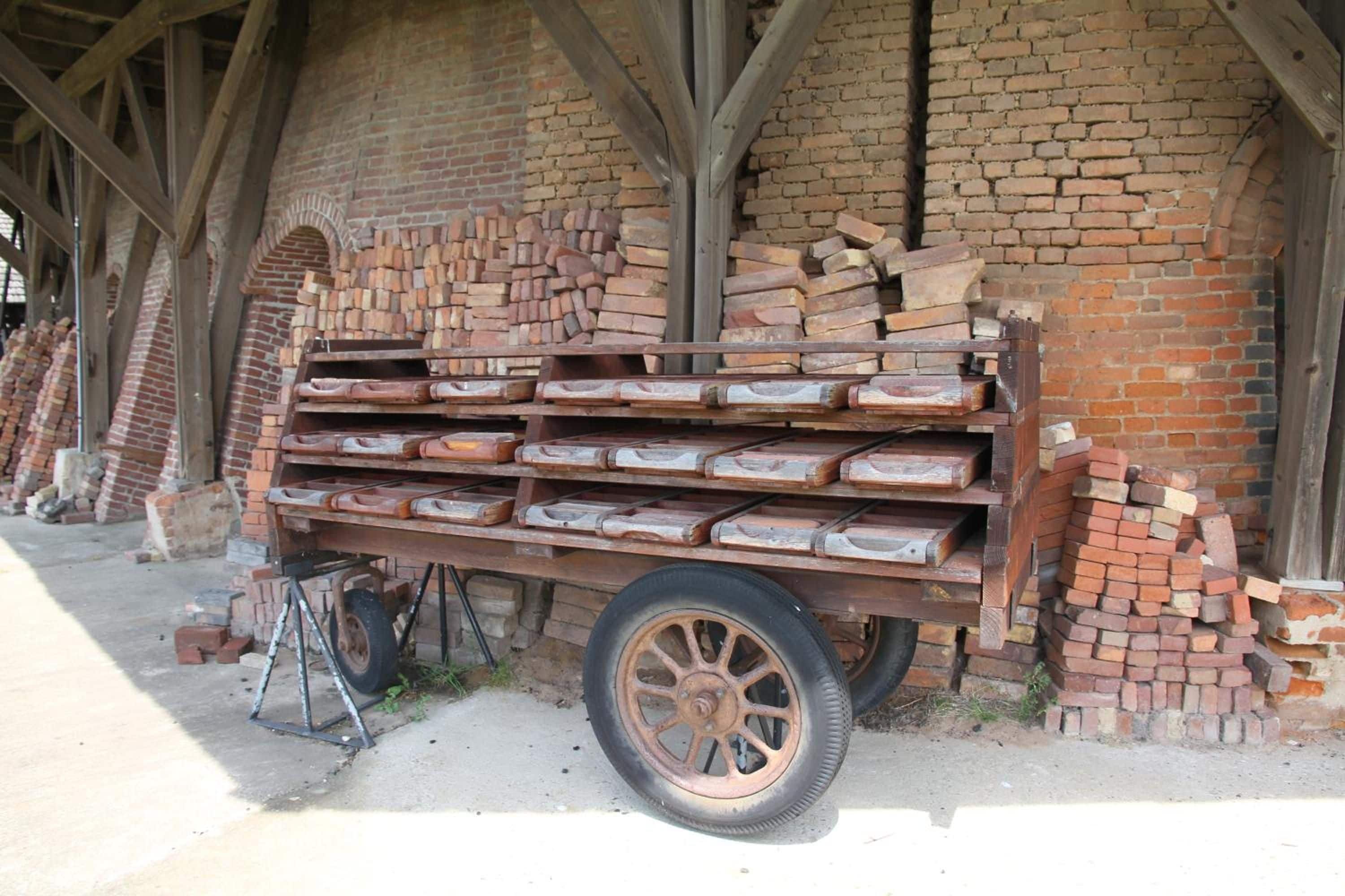 Un carro de madera cargado con ladrillos, estacionado frente a un muro de ladrillo con un ventanal en arco.