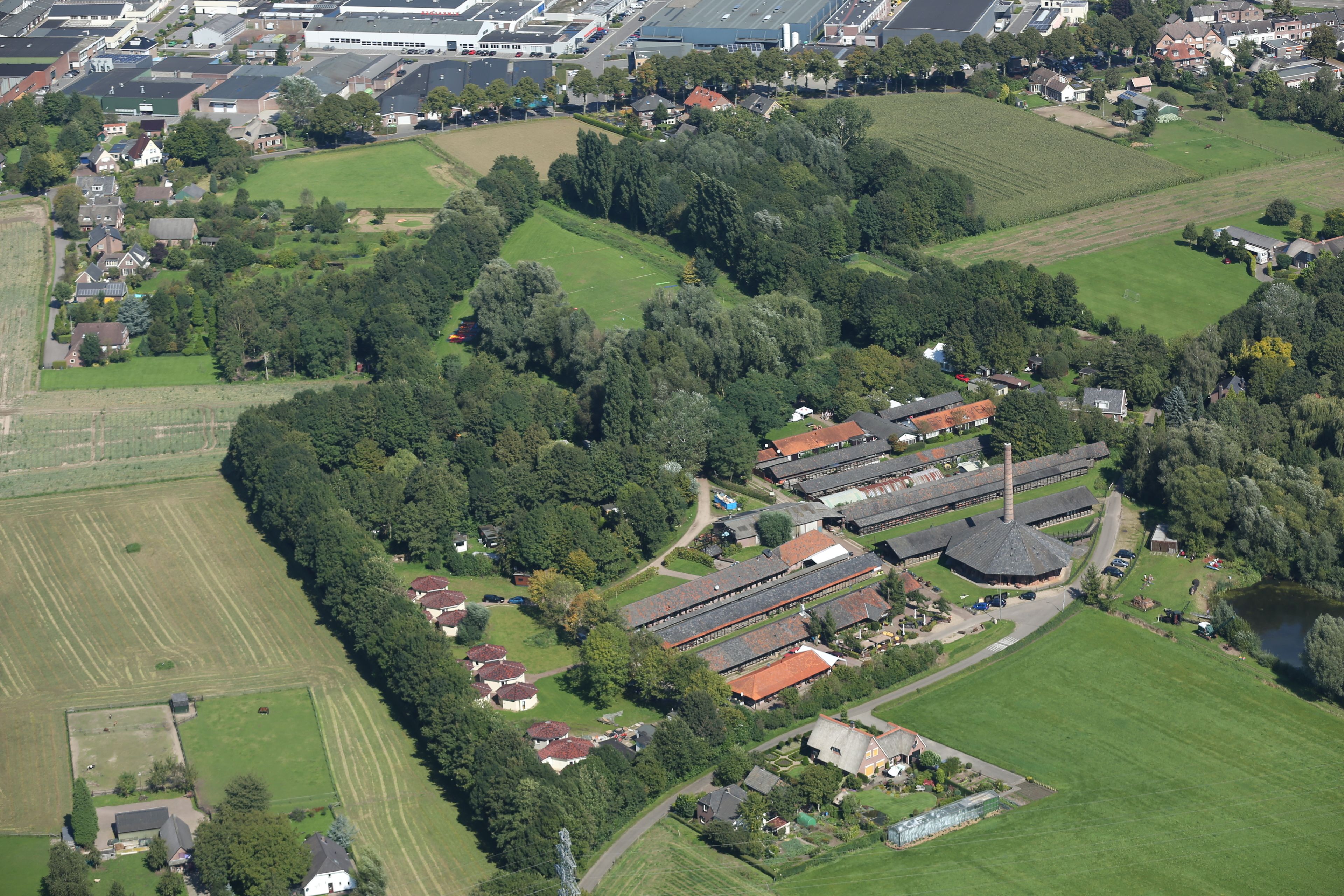 Luchtbeeld van een woongebied met huizen, groene velden en een groot gebouwencomplex.
