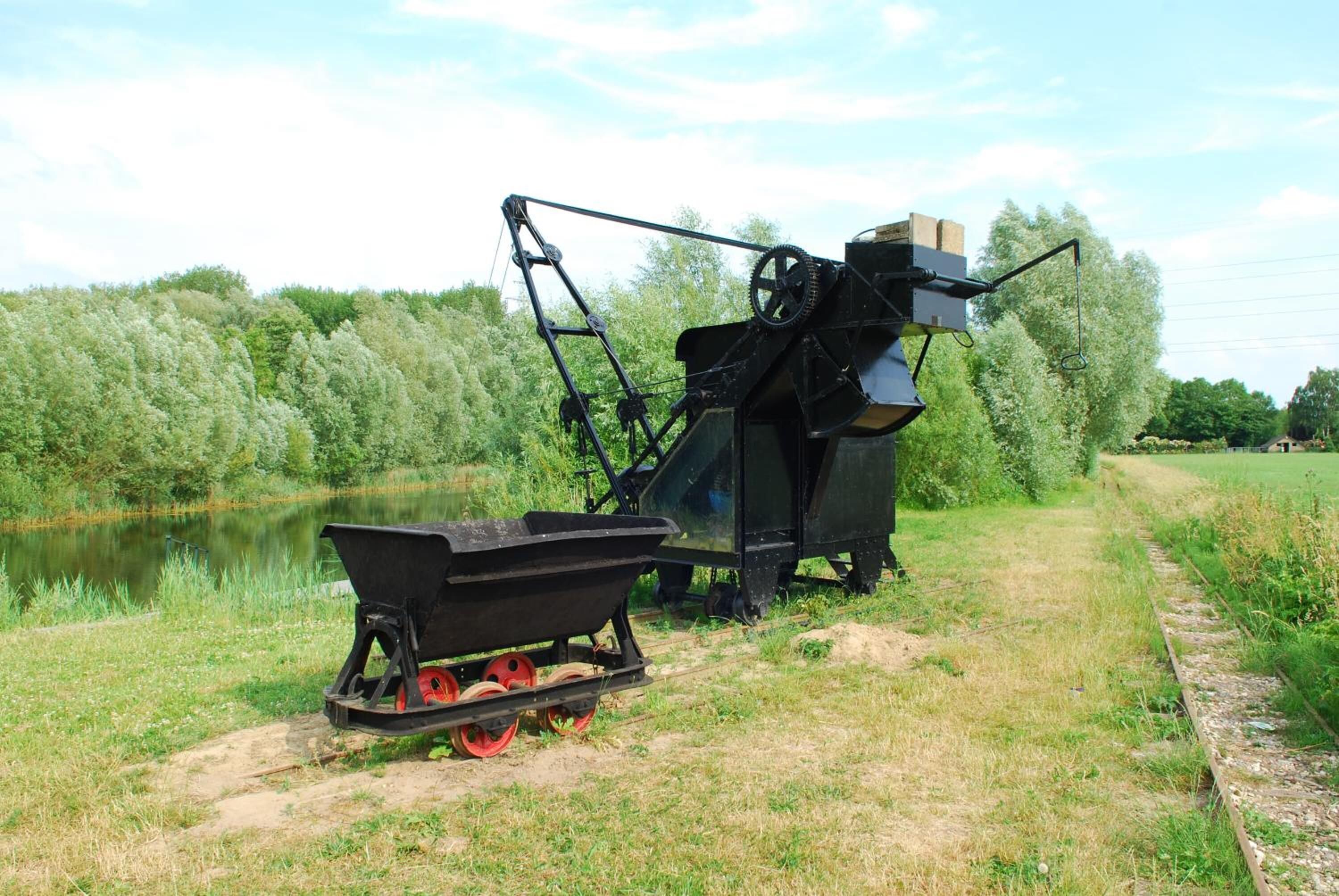 A piece of agricultural machinery with a trailer and a motorized component, situated near a body of water and a grassy area.