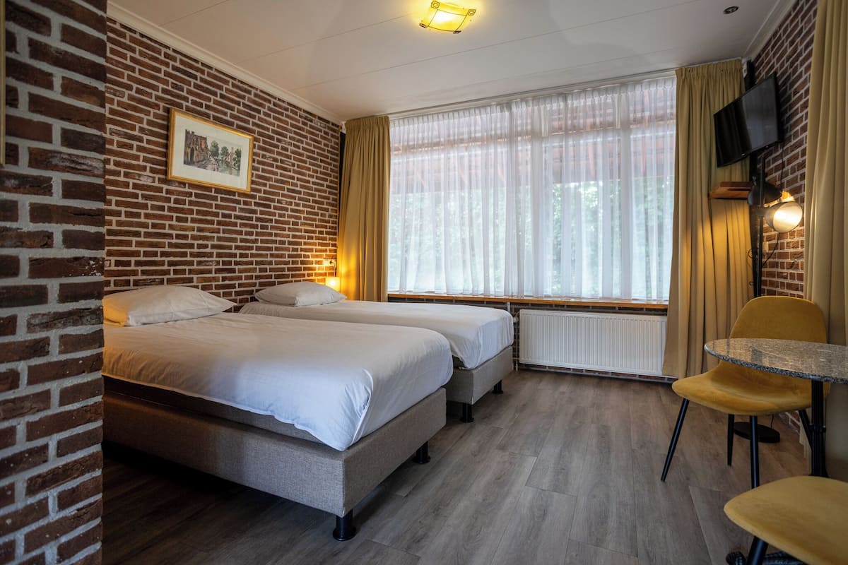 Quarto de hotel com duas camas, uma mesa pequena e uma televisão.