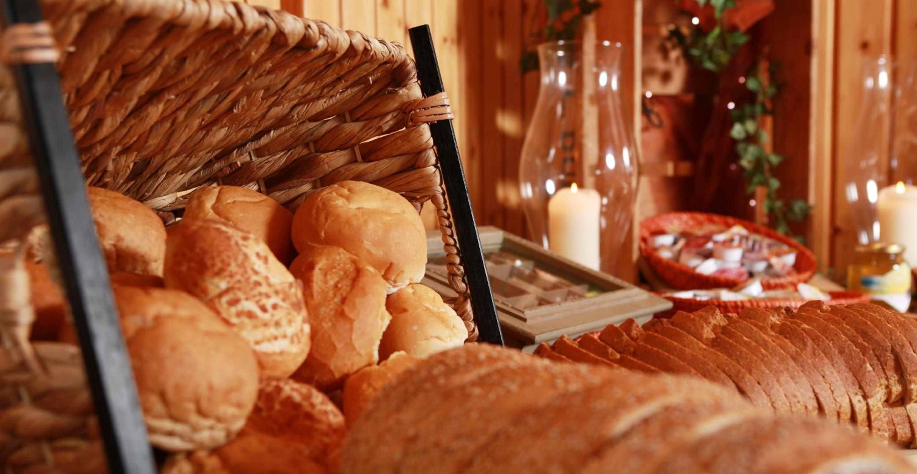 A variety of breads and pastries displayed in a basket and on a table, with candles and a vase in the background.