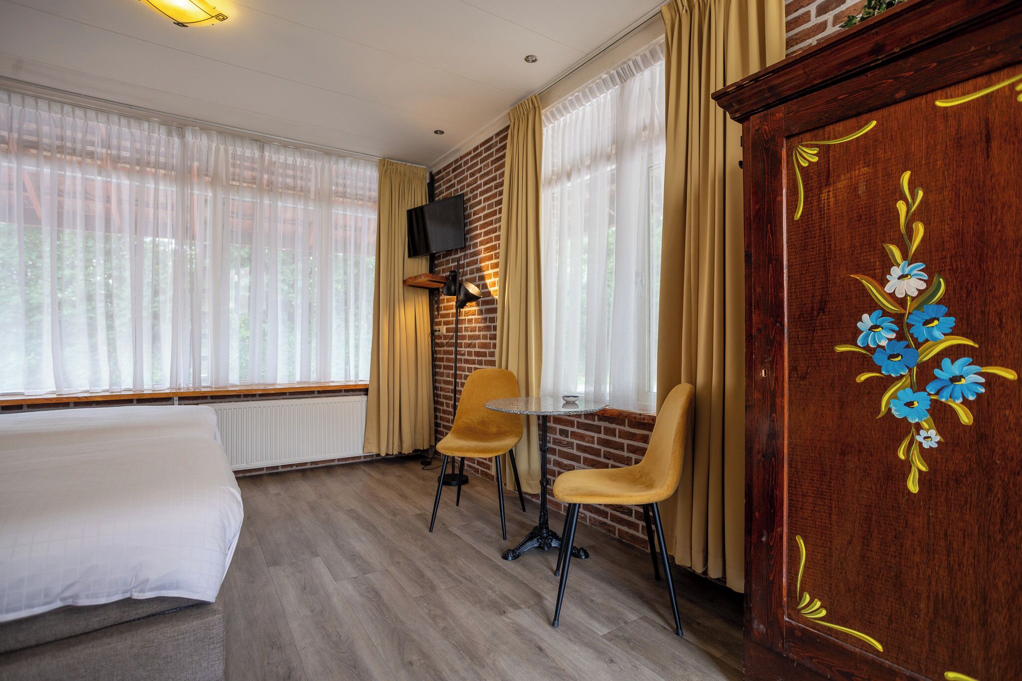 Habitación de hotel con una cama, dos sillones, una mesita, un televisor montado en la pared y un mueble de madera con diseños florales.