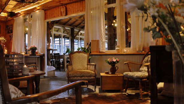 A cozy interior with wooden furniture, a fireplace, and a view through a large window. - Buitengoed de Panoven (Zevenaar)