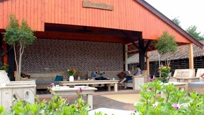 An outdoor seating area with wooden benches and tables, a brick wall, and a wooden pergola. - Buitengoed de Panoven (Zevenaar)