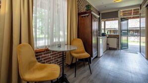 A dining area with two chairs and a small round table, a brick wall, and a view through a glass door to an outdoor area. - Buitengoed de Panoven (Zevenaar)