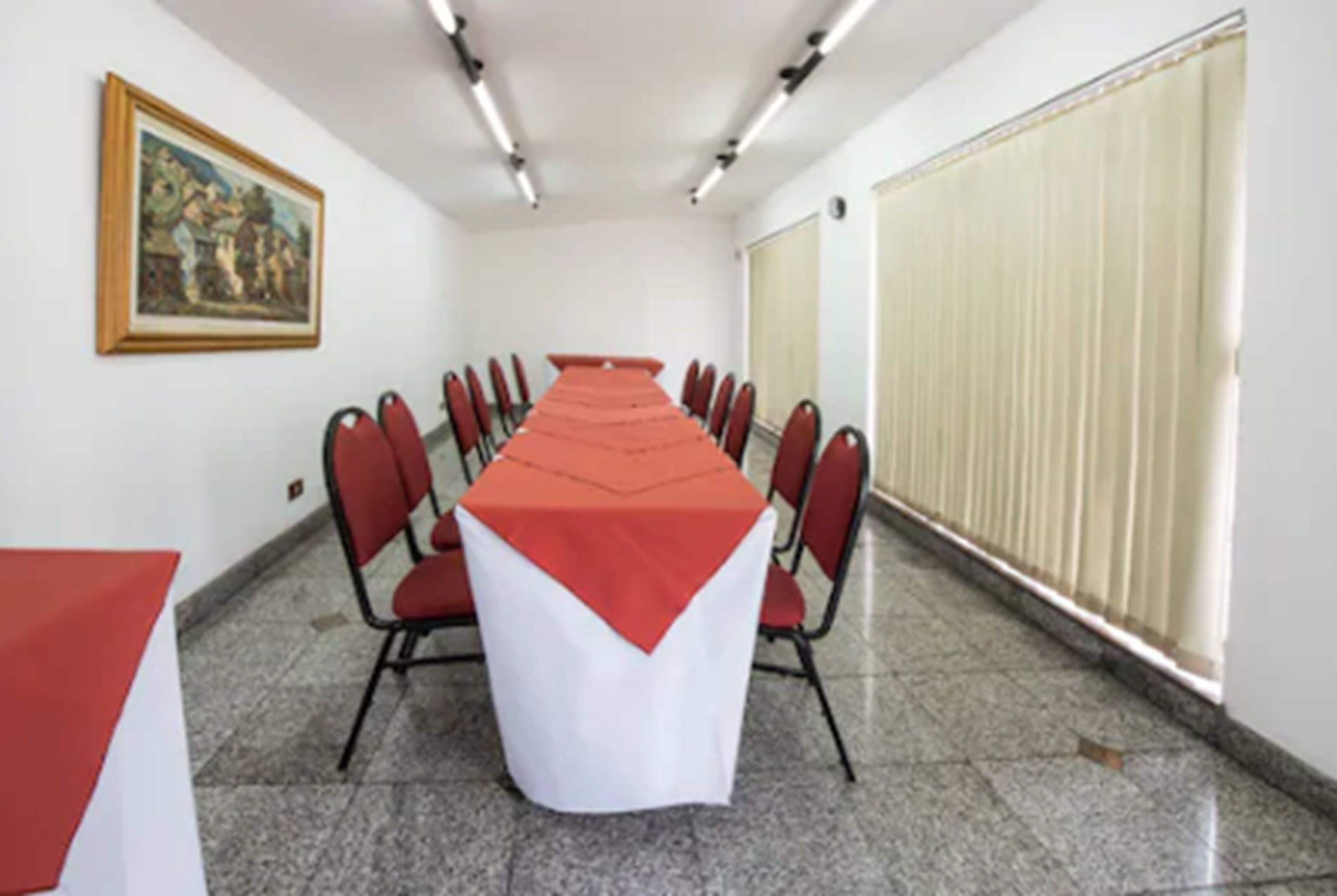 Une salle de conférence avec une longue table, des chaises rouges et une nappe blanche.