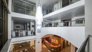 A modern hotel lobby with a central reception desk, a large chandelier, and a mezzanine level with a railing. - Carlton Plaza Poços de Caldas (Poços de Caldas)