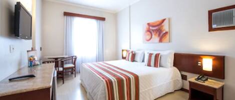 Una habitación de hotel con cama, mesita de noche, televisor y escritorio con sillas.
