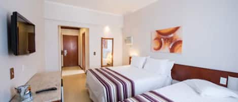 Habitación de hotel con dos camas, televisión, un cuadro y escritorio con lámpara.