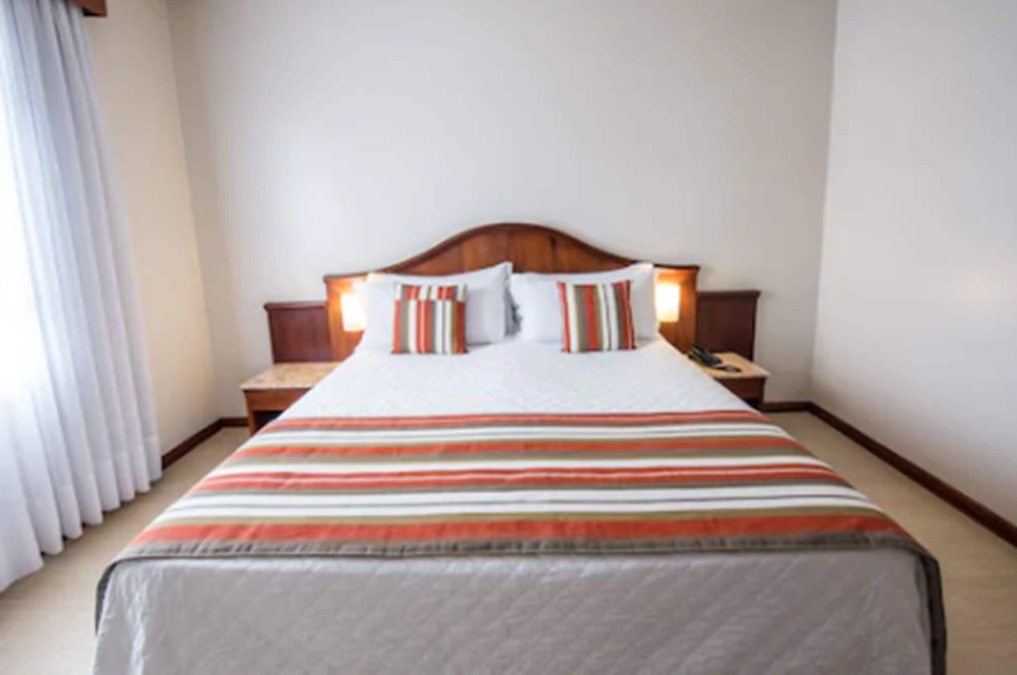A neatly made bed with striped bedding and two bedside tables with lamps.