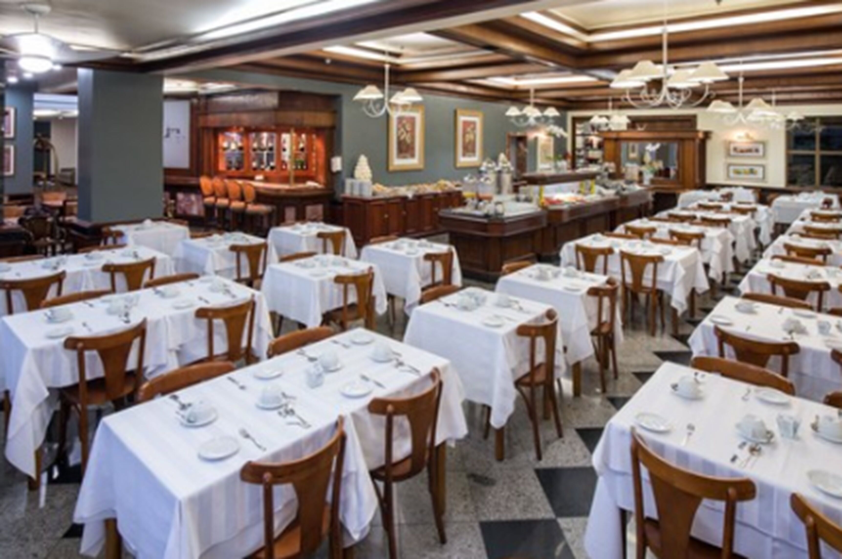 A restaurant with multiple tables set for dining, wooden chairs, and a bar area with stools.