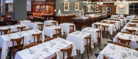 A restaurant with multiple tables set for dining, wooden chairs, and a bar area with stools.