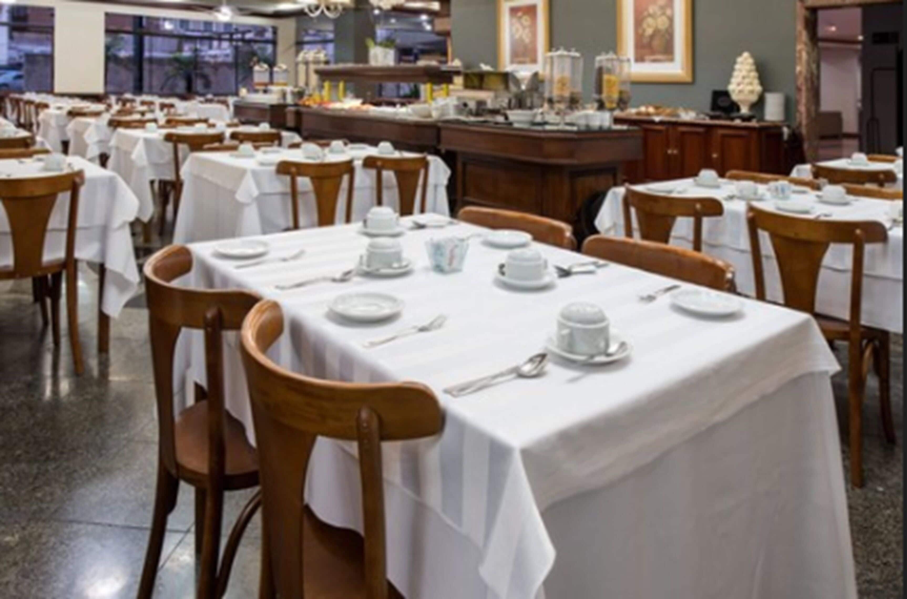 A restaurant with multiple tables set for dining, each with white tablecloths and basic tableware.