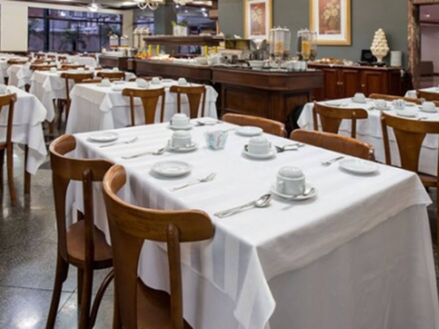 A restaurant with multiple tables set for dining, each with white tablecloths and basic tableware.