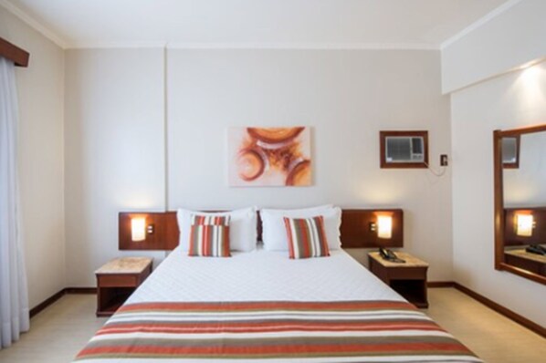 Ein Hotelzimmer mit einem großen Bett, zwei Nachttischen, einem Wandspiegel und einem Bild an der Wand.