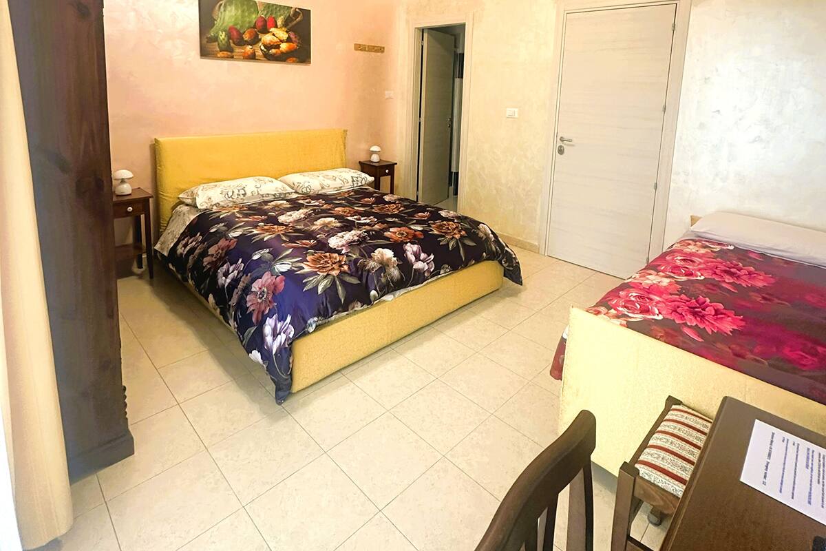 A bedroom with a bed, a desk, a chair, a ceiling fan, a door, and a wall-mounted painting.