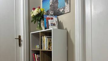 Een boekenplank met boeken en een bloevas, een ingelijst beeld aan de muur, en een deur.