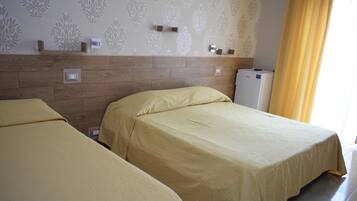 A hotel room with two single beds, a wooden headboard, a small refrigerator, and a wall with a leaf pattern.
