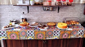 A buffet setup with various food items, a patterned tablecloth, and a brick wall background. - Bed and breakfast delle palme (Trapani)