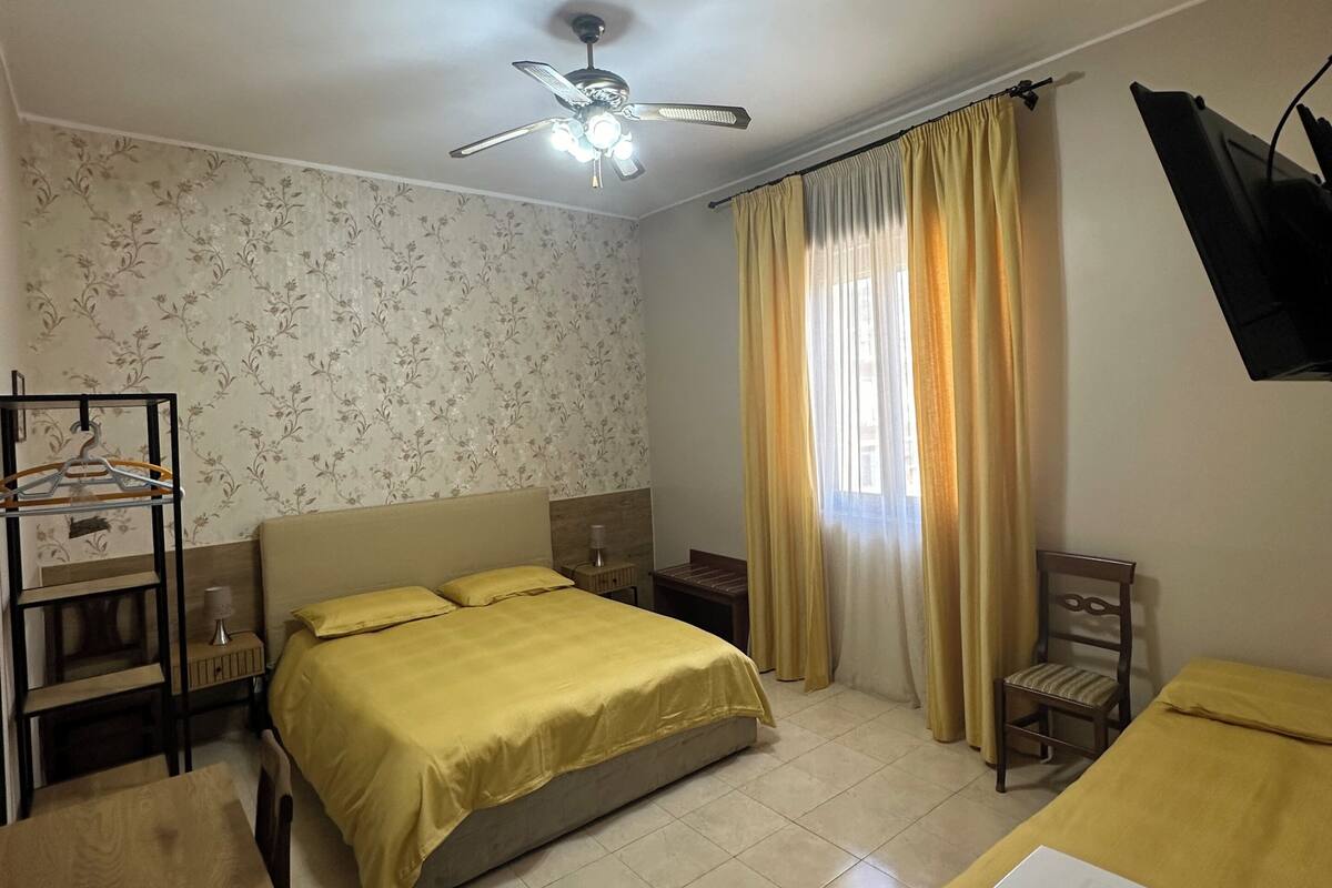 A hotel room with a bed, a desk, a chair, a TV, and a ceiling fan.