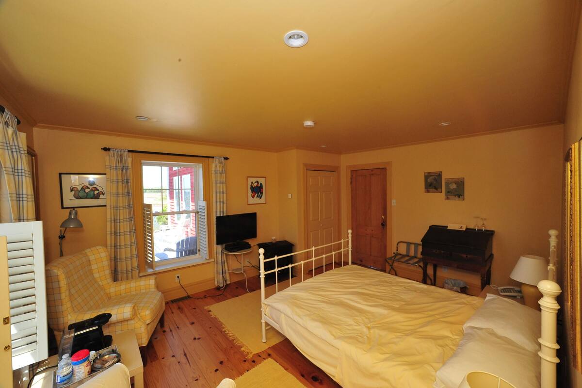 Un dormitorio con cama, una silla, un escritorio, un televisor y una ventana con cortinas.