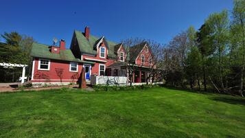 A large red house with a green roof, a porch, and a well-maintained lawn.