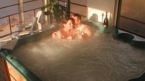 Un bain à remous où se trouvent deux personnes, entouré d’une terrasse en bois et d’une fenêtre.