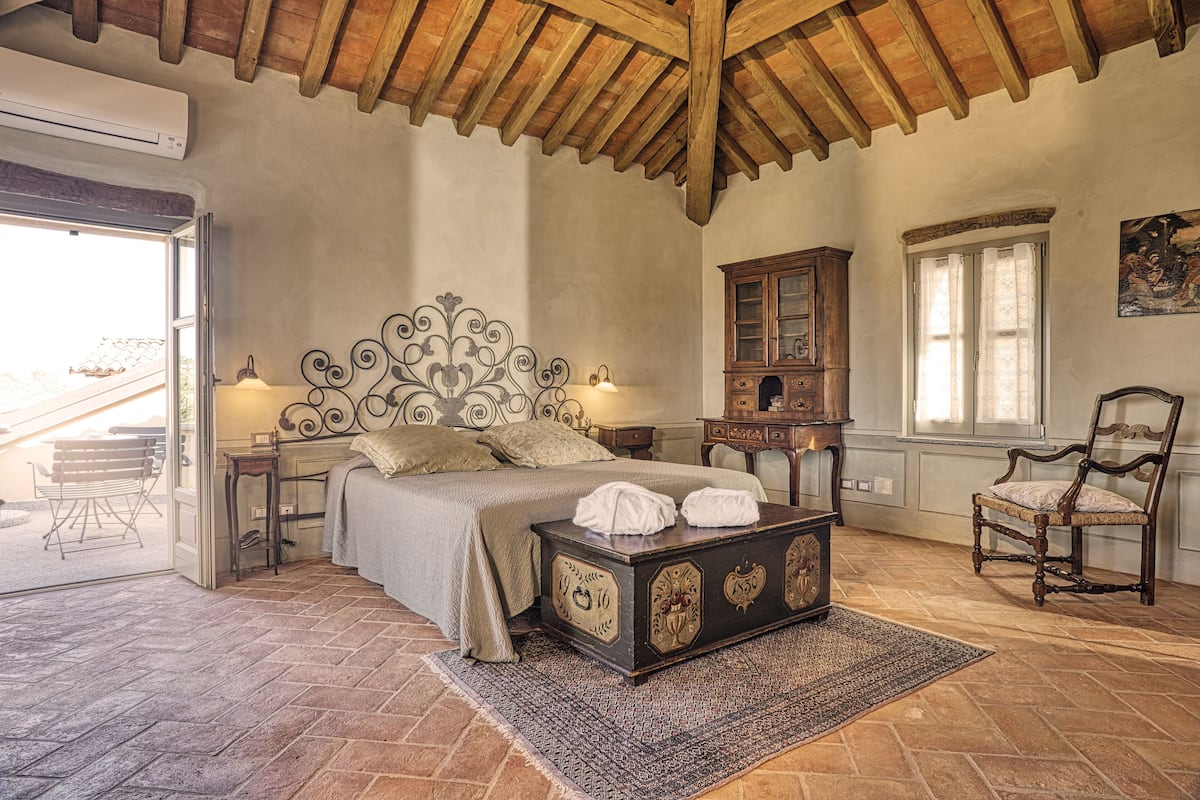 A bedroom with a bed, wooden headboard, a chest of drawers, a chair, and a window.