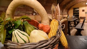 A basket with various vegetables including corn, zucchini, and squash, placed on a table in a rustic setting with brick walls and wooden furniture. - Antica Locanda SanPietro (Govone)