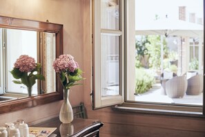 A room with a large window, a wooden floor, a mirror, and a vase with flowers. - Antica Locanda SanPietro (Govone)