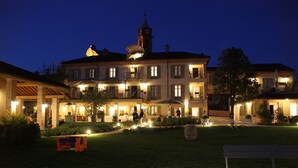 A large, multi-story building with a prominent clock tower, well-lit outdoor areas, and a grassy courtyard with benches. - Antica Locanda SanPietro (Govone)