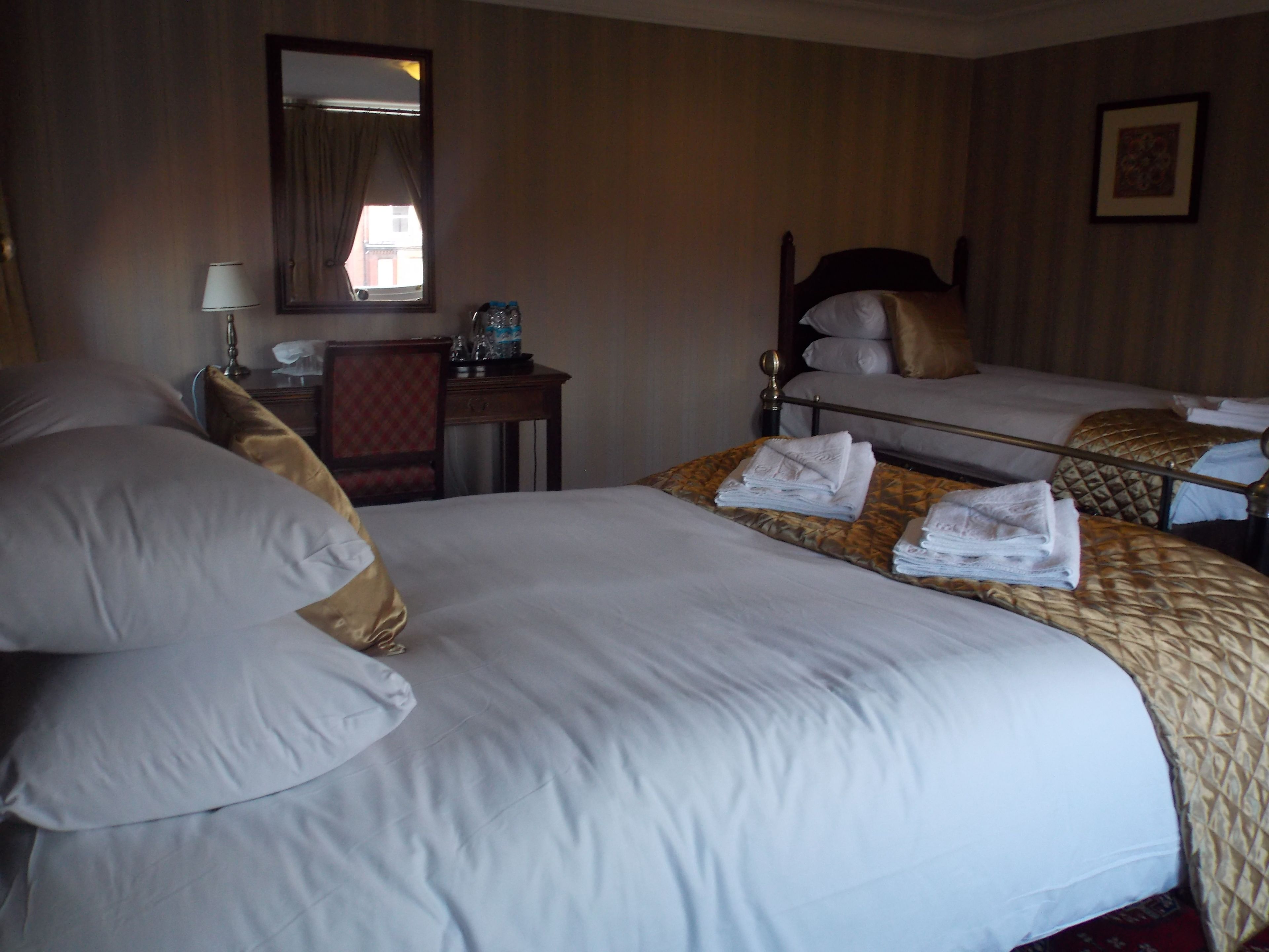 A hotel room with two beds, a desk, a chair, a mirror, and a window with curtains.