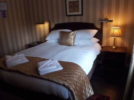 A neatly made bed with white linens and a brown throw blanket, a bedside lamp, and a framed picture on the wall.