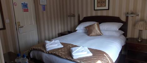 A hotel room with a bed, a nightstand, a lamp, a framed picture on the wall, and a door with a fire action sign.