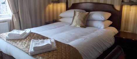 A hotel room with a large bed, a wooden headboard, two bedside tables, and a window with curtains.