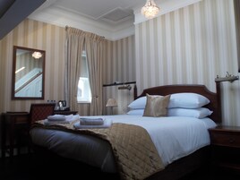 Quarto de hotel com uma cama grande, mesa de cabeceira, espelho e janela com cortinas.