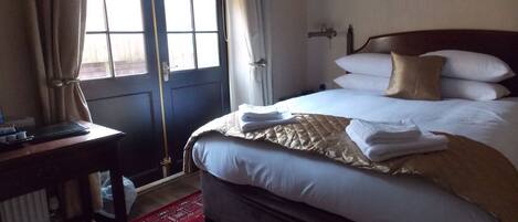 A hotel room with a bed, a desk, a chair, a window with curtains, and a door.
