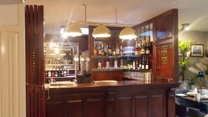 A bar area with wooden paneling, a counter with a cash register, and shelves stocked with bottles and glasses. - The Mountford Hotel - Free Parking (Liverpool)