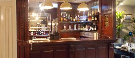 A bar area with wooden paneling, a counter with a cash register, and shelves stocked with bottles and glasses.