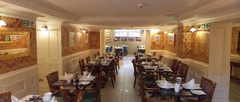 A spacious dining area with multiple tables and chairs, fire exit signs, and framed pictures on the walls.