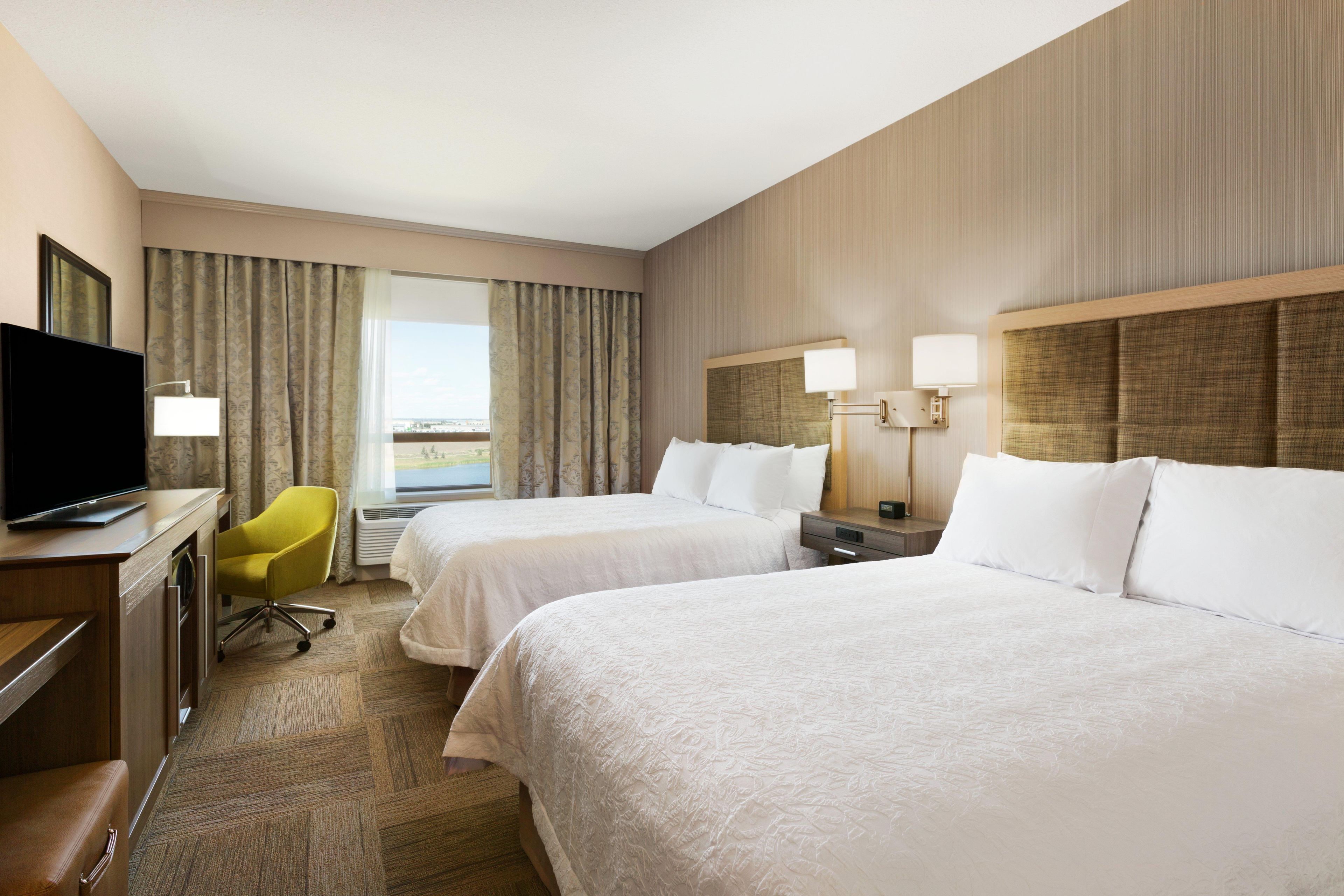Habitación de hotel con dos camas, un escritorio con televisor, una silla y vista al exterior.