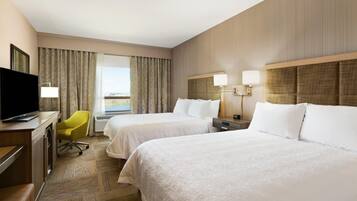 Habitación de hotel con dos camas, un escritorio con televisor, una silla y vista al exterior.