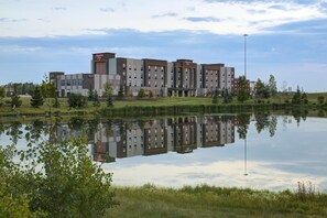 A multi-story hotel with a reflection in a calm body of water, surrounded by greenery.