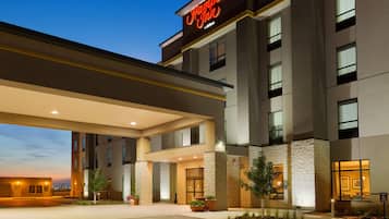 A Hampton Inn hotel entrance with a modern design, large windows, and a well-lit facade.