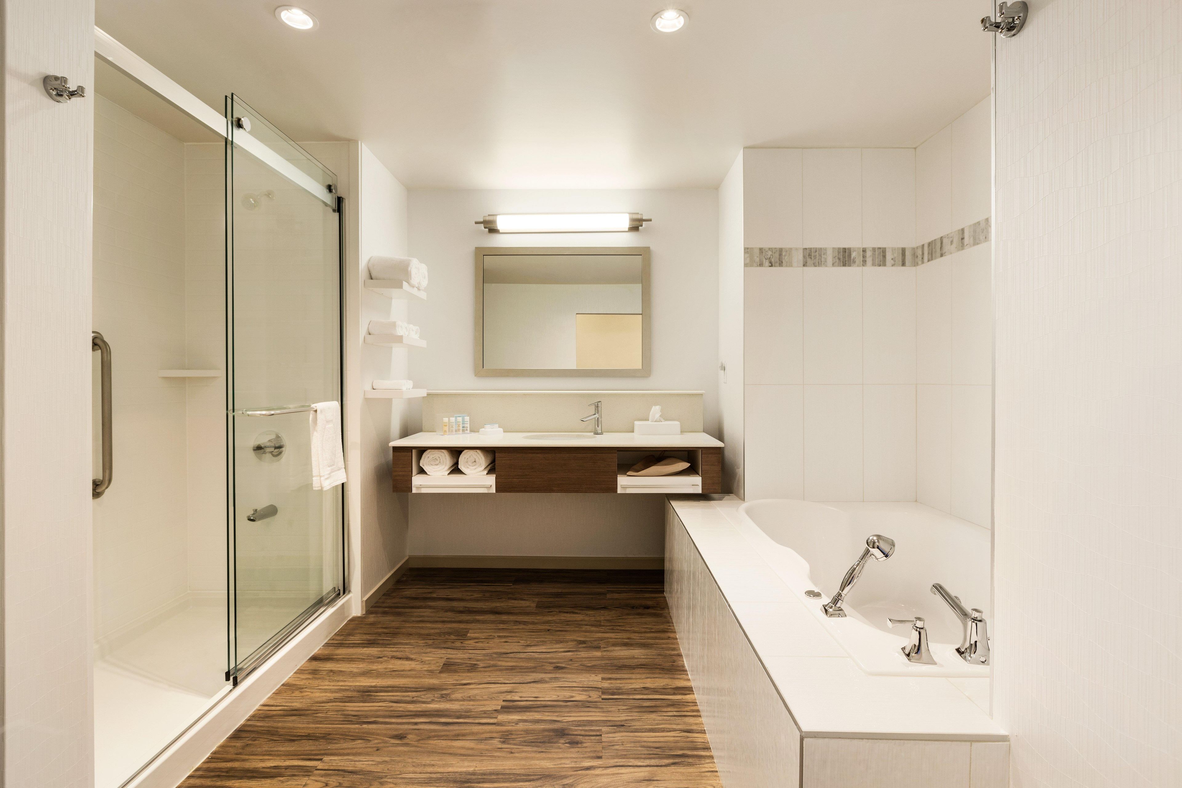A modern bathroom with a glass shower enclosure, a wooden floor, a white sink, and a large bathtub.