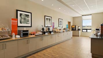 Un espace moderne dédié au petit-déjeuner, avec un long comptoir, des machines à café et des tableaux encadrés accrochés au mur.