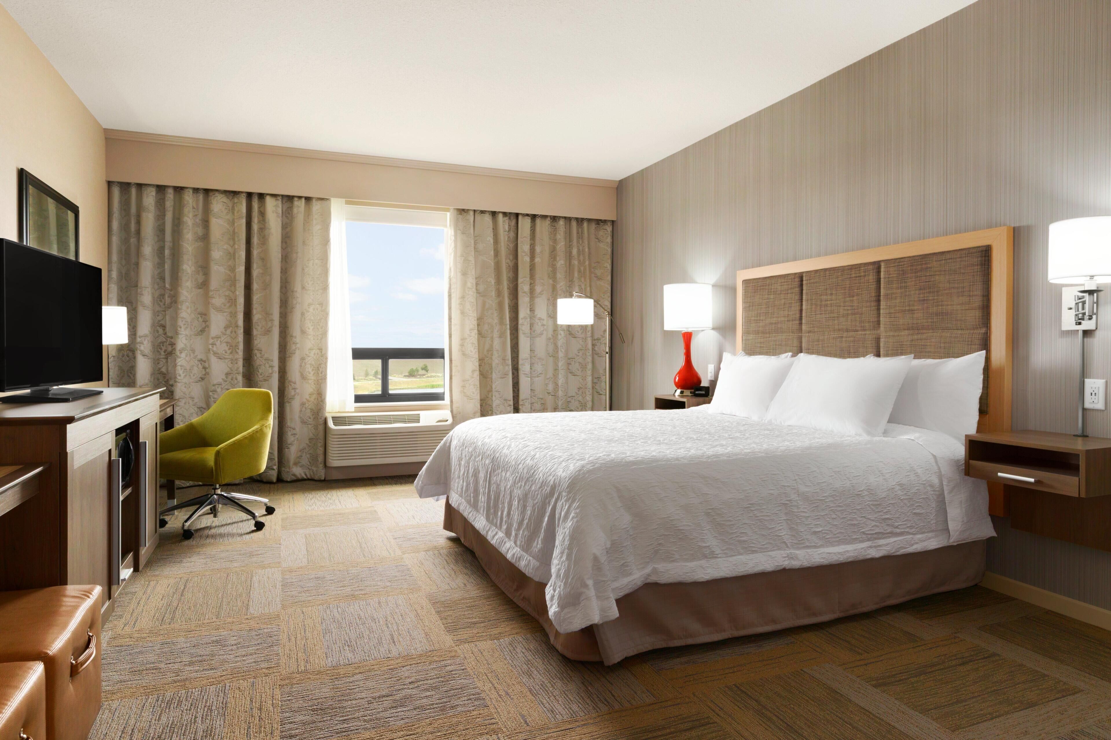 A hotel room with a bed, a desk with a television, a chair, and a window with curtains.