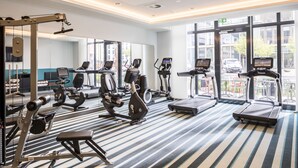 A modern gym with various exercise equipment, large windows, and a striped floor.